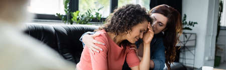 lesbian woman hugging crying african american girlfriend during appointment with psychologist,...