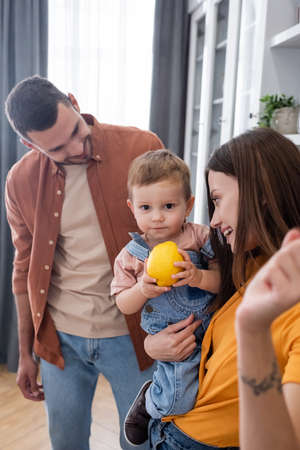 Toddler boy holding lemon near smiling parents at home