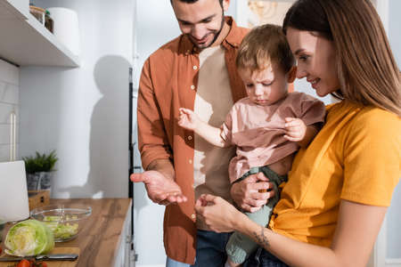 Happy parents looking at kid near vegetables on kitchen worktopの写真素材