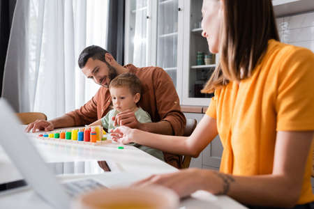 Father and child playing with educational game near mother using laptopの写真素材