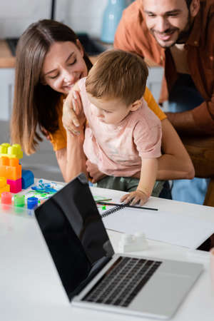 Laptop near smiling family, sketchbook and building blocks at home