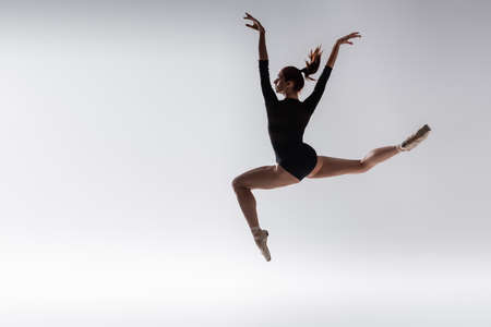 full length of young ballerina in black bodysuit levitating on greyの写真素材