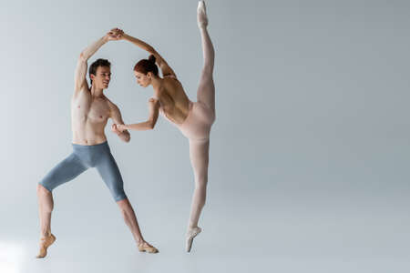 full length of young cheerful ballet dancer performing ballet dance with ballerina on greyの写真素材