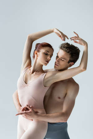 shirtless man and young woman with raised hands performing ballet dance isolated on greyの写真素材