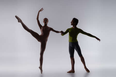 silhouette of dancer holding hands with ballerina on greyの写真素材