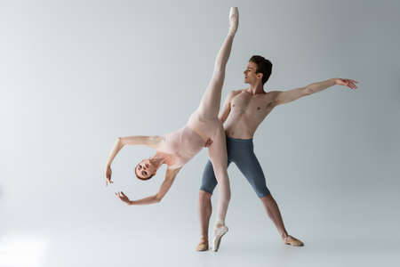 shirtless ballet dancer supporting flexible ballerina with outstretched hands isolated on greyの写真素材
