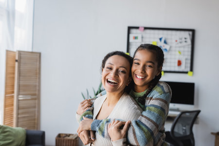 excited african american girl embracing mother while looking at cameraの写真素材