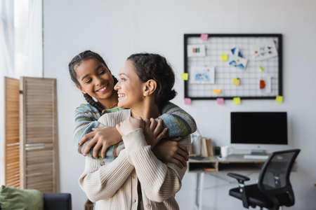 cheerful african american mother and daughter looking at each other while embracing at homeの写真素材