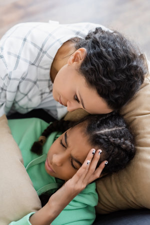 top view of african american woman calming teenage daughter lying with closed eyes and suffering from headacheの写真素材