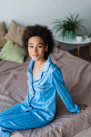 Young african american woman in pajamas looking at camera on bedの写真素材