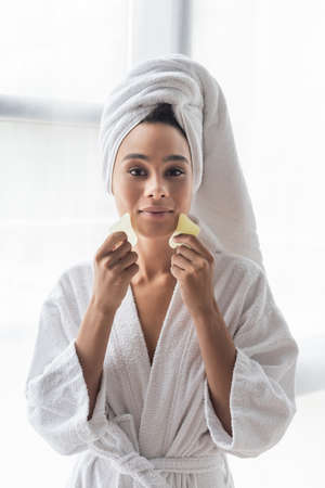 young african american woman in white towel scrapping face with face scrapersの写真素材