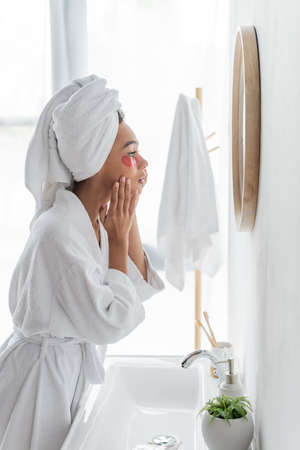 side view of african american woman applying eye patch while looking at mirrorの写真素材