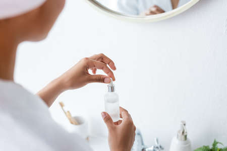 partial view of young african american woman holding bottle with serum in bathroomの写真素材