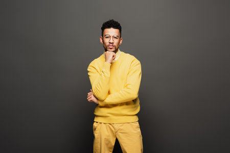 serious african american man in yellow outfit and glasses looking at camera on dark grey