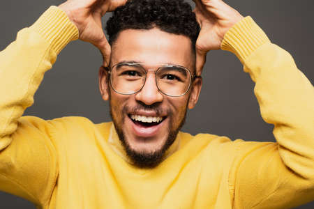 amazed african american man in glasses smiling isolated on grey