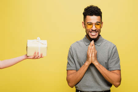 cheerful african american man in sunglasses near woman holding wrapped present isolated on yellow