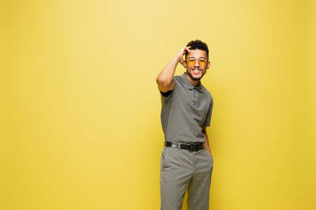 happy african american man in sunglasses and grey tennis shirt isolated on yellowの写真素材