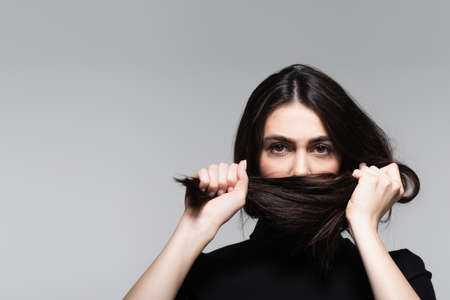 young woman covering mouth with brown hair isolated on greyの写真素材