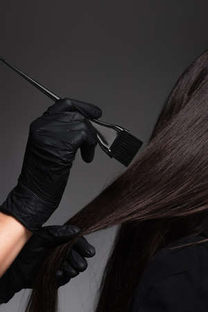 partial view of colorist holding brush near woman with brown hair isolated on dark greyの写真素材