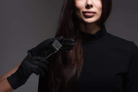 cropped view of hairstylist holding brush near woman with brown hair isolated on dark grey