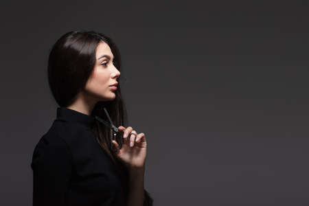 side view of young woman in black turtleneck holding scissors near long shiny hair isolated on dark greyの写真素材