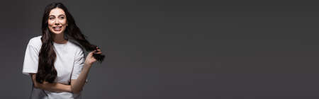 young happy woman adjusting wavy hair on dark grey, bannerの写真素材