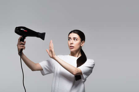 careful woman in white t-shirt holding hair dryer isolated on greyの写真素材
