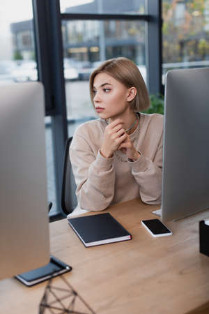 young blonde manager working near computer monitors in modern office