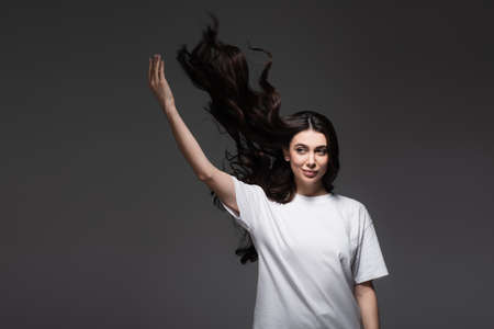 smiling young woman with wavy hair and raised hand on dark greyの写真素材