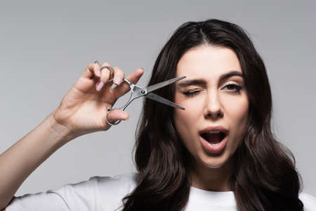 woman with open mouth and wavy hair holding scissors isolated on greyの写真素材