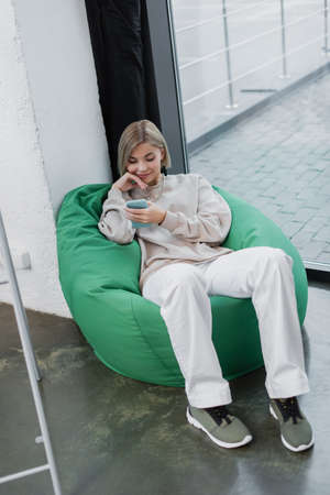 happy manager sitting in bean bag chair and using smartphoneの写真素材