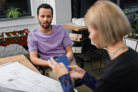 african american interior designer looking at blurred blonde colleague with sample