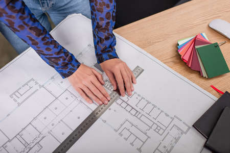 top view of interior designer holding ruler while working with blueprint near colorful samplesの写真素材