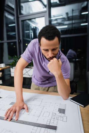 pensive african american architect holding pencil and ruler near blueprintの写真素材