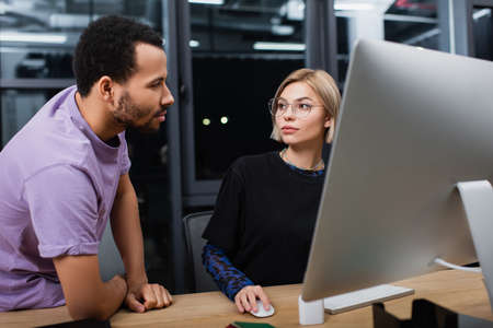 blonde manager in glasses using computer near african american colleague