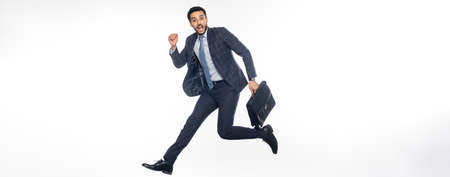 positive businessman in suit jumping with briefcase on white, bannerの写真素材