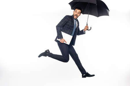 excited businessman in suit jumping with laptop and umbrella on whiteの写真素材