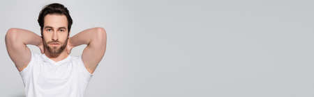 brunette man in white t-shirt posing with hands behind neck isolated on grey, bannerの写真素材