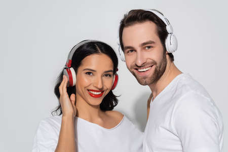cheerful young couple in headphones looking at camera while listening music on grey