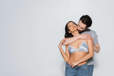 sexy woman in jeans and bra near brunette man hugging her on greyの写真素材