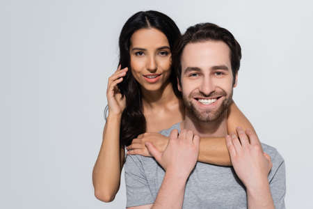 pretty brunette woman looking at camera while hugging bearded man in t-shirt  isolated on grey