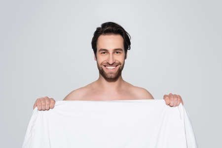 brunette shirtless man smiling at camera behind white blanket isolated on greyの写真素材