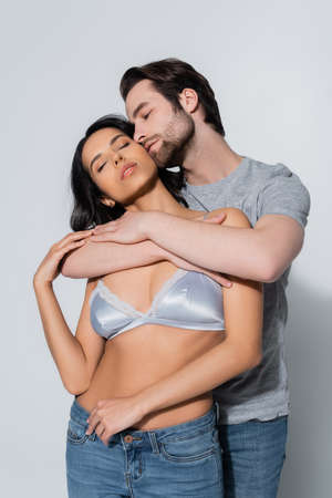 young man hugging sexy girl in satin bra standing with closed eyes on greyの写真素材