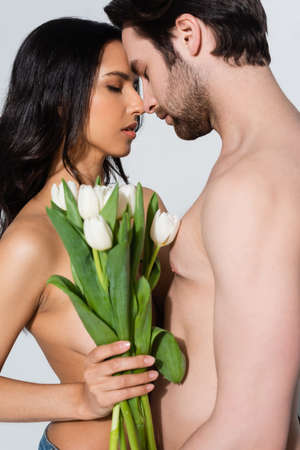 nude young woman and shirtless man standing with closed eyes near tulips on greyの写真素材