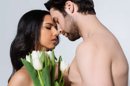 young couple with closed eyes standing near tulips isolated on grey