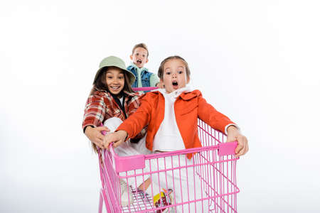 joyful kids riding in pink shopping cart on whiteの写真素材