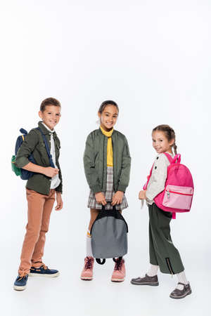 happy schoolboy and cheerful schoolgirls standing with backpacks on whiteの写真素材
