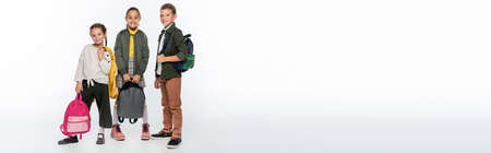 cheerful schoolboy and joyful schoolgirls standing with backpacks on white, bannerの写真素材