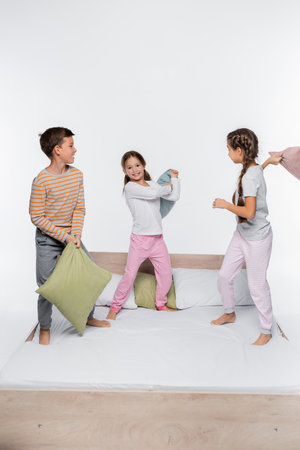 happy kids having pillow fight while standing isolated on whiteの写真素材