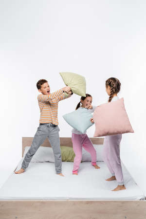playful kids in pajamas having pillow fight while standing isolated on whiteの写真素材